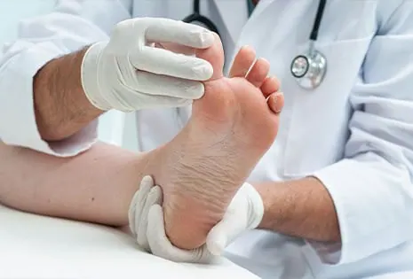 A podiatrist in white gloves checking the sole of a patient's foot