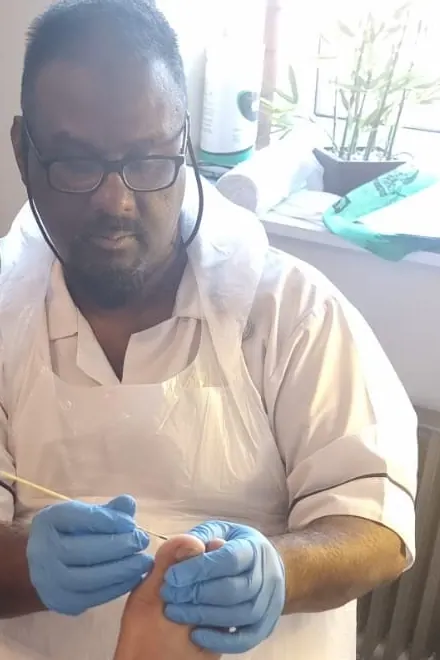 Ray treating a patient's foot in the clinic, wearing gloves and an apron